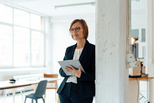 Businesswoman With Tablet PC Leaning On Column In Office