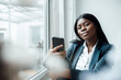 © Westend61 - Businesswoman holding smart phone sitting by window in office