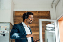 Happy Businessman Talking On Smart Phone Through Wireless Headset In Office