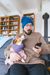 © Westend61 - Shocked man with wooly hat sitting on couch holding dog checking smartphone