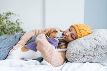 Woman Wearing Warm Clothing Cuddling With Dog In Bed