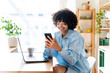 © Westend61 - Happy young woman using smart phone sitting at kitchen island
