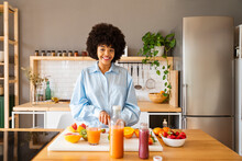 Happy Beautiful Woman With Fruits Standing In Kitchen At Home