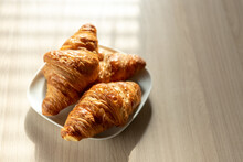 There Are Three Croissants On The Table On A White Plate For Breakfast
