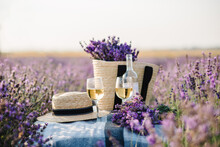 Two Glasses With White Wine And Bottle On Background Of A Lavender Field. Straw Hat And Basket With Flowers Lavender On A Blanket On Picnic. Romantic Evening In Sunset Rays. Summer In Provence, France