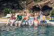 © Carlo - group of friends sitting by the poolside celebrating and rejoicing the pool party together raising beer bottles