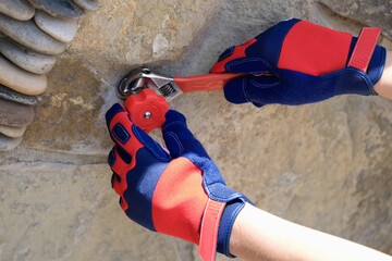 Person hands in work gloves repairing tap using wrench