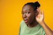 Dark-skinned woman on a yellow background overhears a conversation