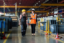 Two Young Workers Of Modern Industrial Factory Having Discussion Of Work While Moving Along Aisle Between New Equipment