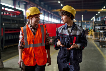 Aufkleber - Two young female workers of modern factory discussing working points while moving down large workshop or distribution warehouse