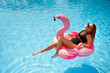 © artiemedvedev - Hot slim woman relaxing on inflatable pink flamingo float mattress in bikini at swimming pool. Attractive fit girl in swimwear lies in the sun on floaty. Pretty female chilling on tropical vacation.