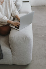 Wall Mural - Young woman works on laptop sitting on comfortable sofa. Elegant person hands working on laptop computer. Aesthetic bohemian home office workspace. Work at home. Flat lay, top view