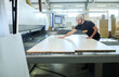 © pressmaster - Young workman in uniform putting wooden boards on modern equipment during work at furniture factory