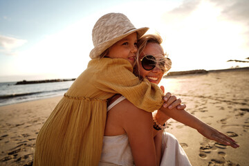 Happy mother with her little daughter having fun together on the beach, playing and hugging. Family summer vacations. Mother's day. Children's day.