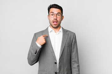 young adult hispanic man looking shocked and surprised with mouth wide open, pointing to self. business concept