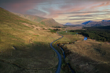 Wall Mural - A country side winding road near the Glenlosh Valley in county Galway, Ireland, with mountains in the background