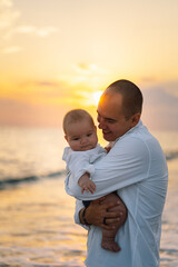 Wall Mural - Happy Father's day. Father and baby play on the beach. Dad and him Child together enjoying sunset. Loving single father hugs cute little son.