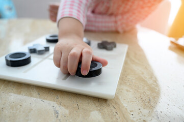 Closeup hand of child little girl playing Tic Tac Toe or OX board game on marble table, top view.