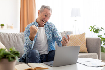 Wall Mural - Mature man using cellphone celebrating success shaking fists screaming yes