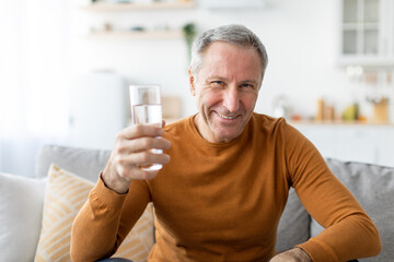 Wall Mural - Smiling mature man sitting on couch holding glass of water