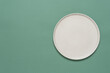 © Yulia - Empty beige plate on green pastel paper background. Top view, flat lay.