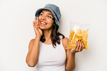 Wall Mural - Young hispanic woman holding a bag of chips isolated on white background shouting and holding palm near opened mouth.