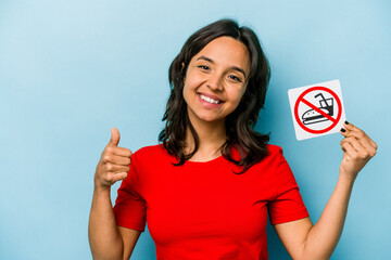 Wall Mural - Young hispanic woman holding no eating sign isolated on blue background smiling and raising thumb up