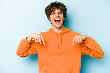 Wall Mural - Young caucasian man isolated on blue background points down with fingers, positive feeling.