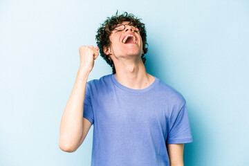 Wall Mural - Young caucasian man isolated on blue background celebrating a victory, passion and enthusiasm, happy expression.