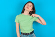 © Roquillo - young beautiful Caucasian woman wearing green T-shirt over blue wall stressed, anxious, tired and frustrated, pulling shirt neck, looking frustrated with problem