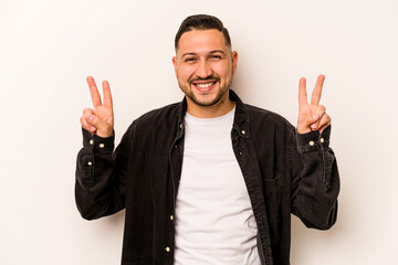 Young hispanic man isolated on white background showing victory sign and smiling broadly.