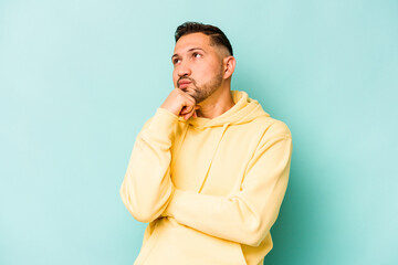 Wall Mural - Young hispanic man isolated on blue background thinking and looking up, being reflective, contemplating, having a fantasy.