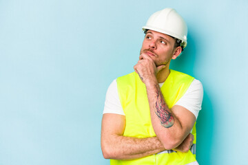 Young laborer caucasian man isolated on blue background looking sideways with doubtful and skeptical expression.
