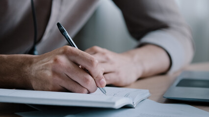 Close up unknown right-handed male business man write notes business ideas at organizer writer sit at home office hold pen notice information tasks in dairy making appointments self-education concept