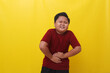 Asian boy standing holding stomach feeling hungry. Isolated on yellow background