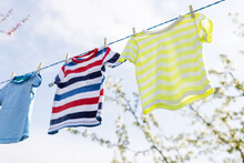 Clean Clothes On Rope Outdoors On Laundry Day. Colorful T-shirts Hanging On A Laundry Line Against Blue Sky