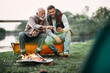 © Drazen - Happy senior father and his son using smart phone by bonfire while camping in nature.