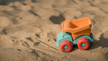 Children's Plastic Toy In The Sandbox. Toy Truck Orange And Blue Color.