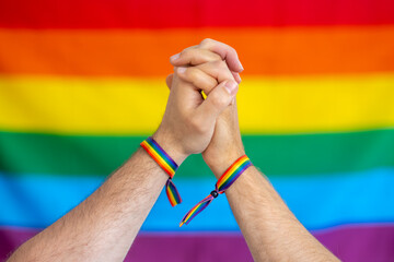 Pareja con las manos unidas y con pulseras con la bandera lgtbi , sobre fondo con la bandera del colectivo lgtbi