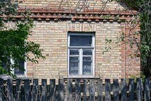 Brown Brick Wall Of A Private Rural House With A White Window Behind A Gray Wooden Fence On The Street