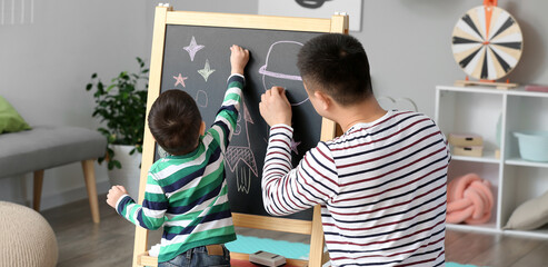 Poster - Happy Asian man and his little son drawing on chalkboard at home