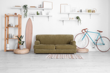 Interior of stylish living room with sofa, bicycle and shelves near white wall