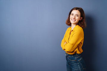 Wall Mural - Laughing young woman stands with crossed arms in front of blue background and laughs into camera