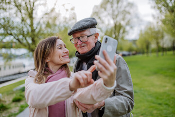 Wall Mural - Happy senior man and his adult daughter taking selfie outdoors on a walk in park.