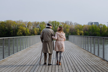 Wall Mural - Rear view of senior man with daughter outdoors on a walk on pier by river.