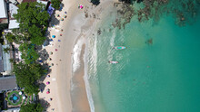 The Snow-white Kata Beach Of Phuket Island. Top View From A Drone On The Ocean Waves. There Are Several Thai Boats. The Whole Island Is Green. The Water Is Clear And Transparent. People Are Bathing