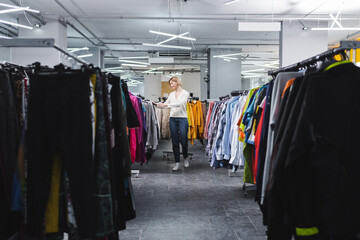 Side view of smiling woman walking near clothes in second hand.