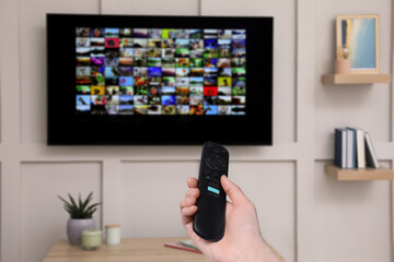 Wall Mural - Woman with remote control changing channels while watching TV at home, closeup