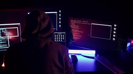 Hacker among many monitors in a dark room