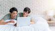 © Pitchayaarch - Happy gay asian couple lying on a bed using laptop computer.